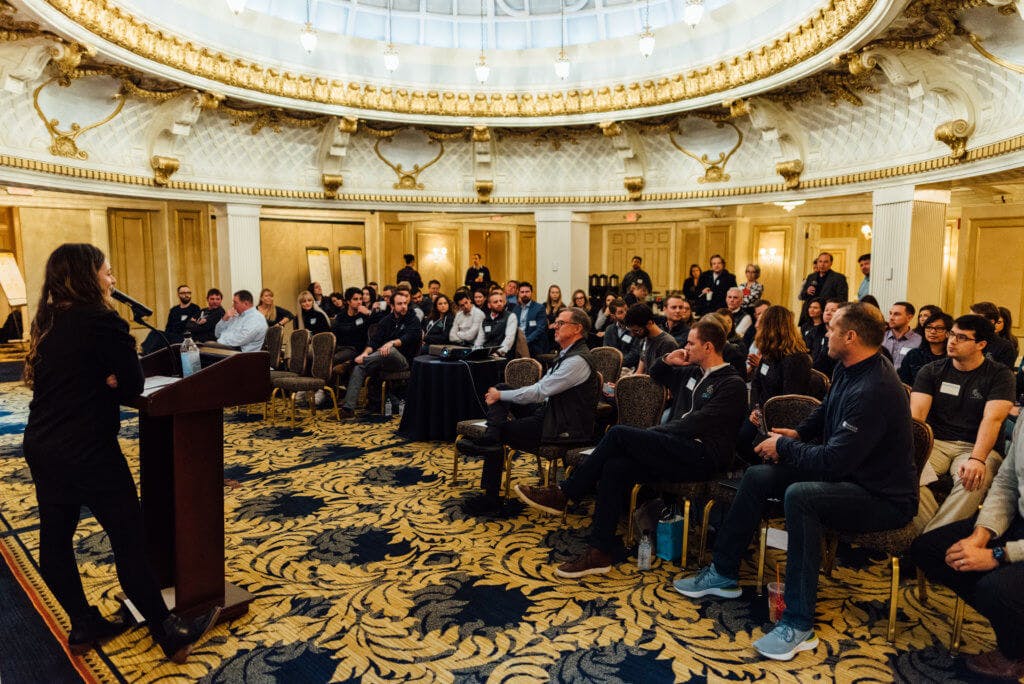 A person presenting in-front of a large room full of people sitting