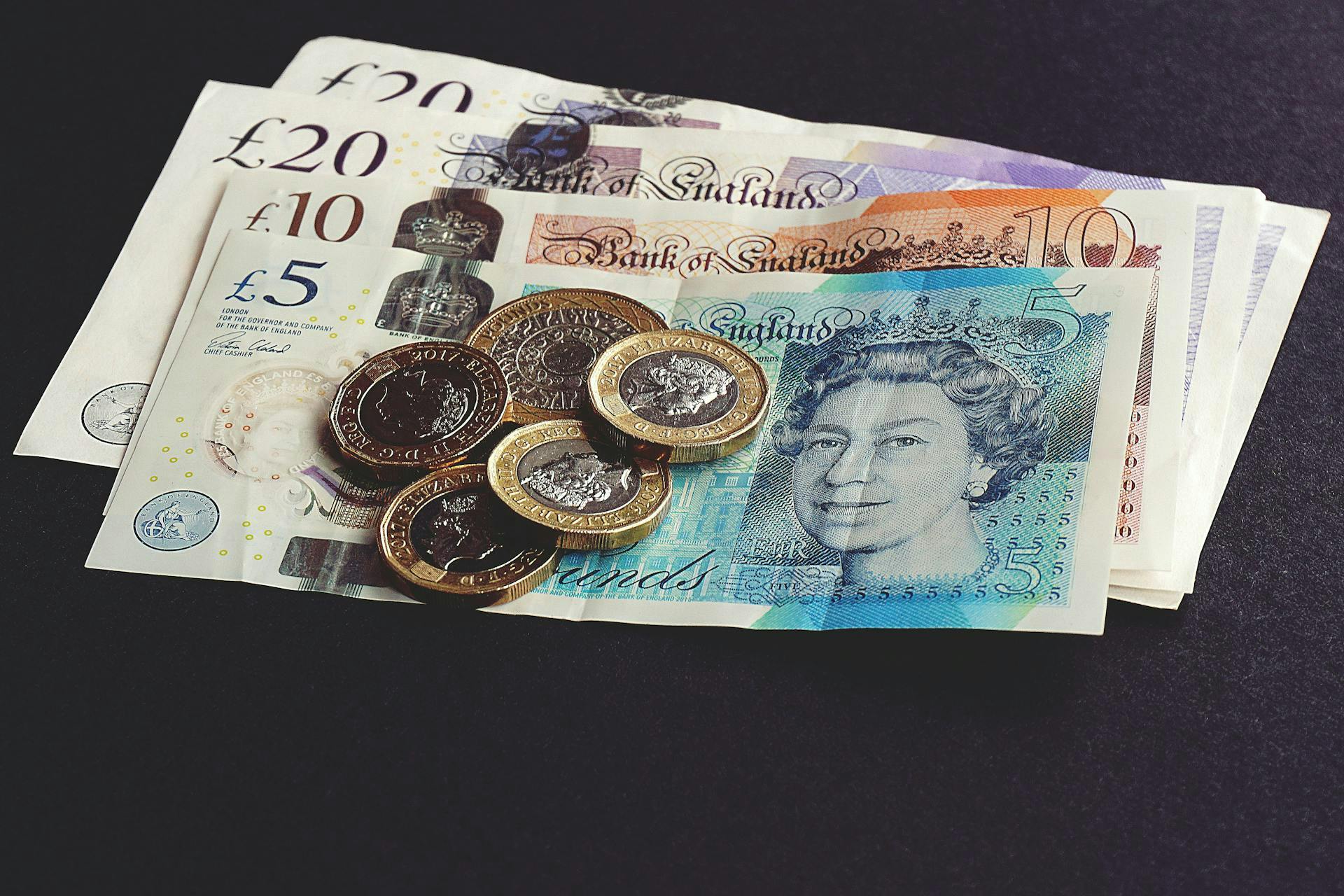 Some British Pound notes and coins on a black background.